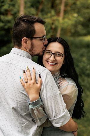 Romantic engagement photo showing couple embracing with bright smiles in woodland setting.