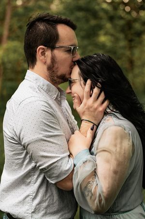 Intimate moment between couple in white and sage clothing embracing in forest setting.