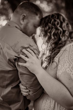 A romantic black and white portrait captures an intimate embrace between a couple in lace and formal attire.