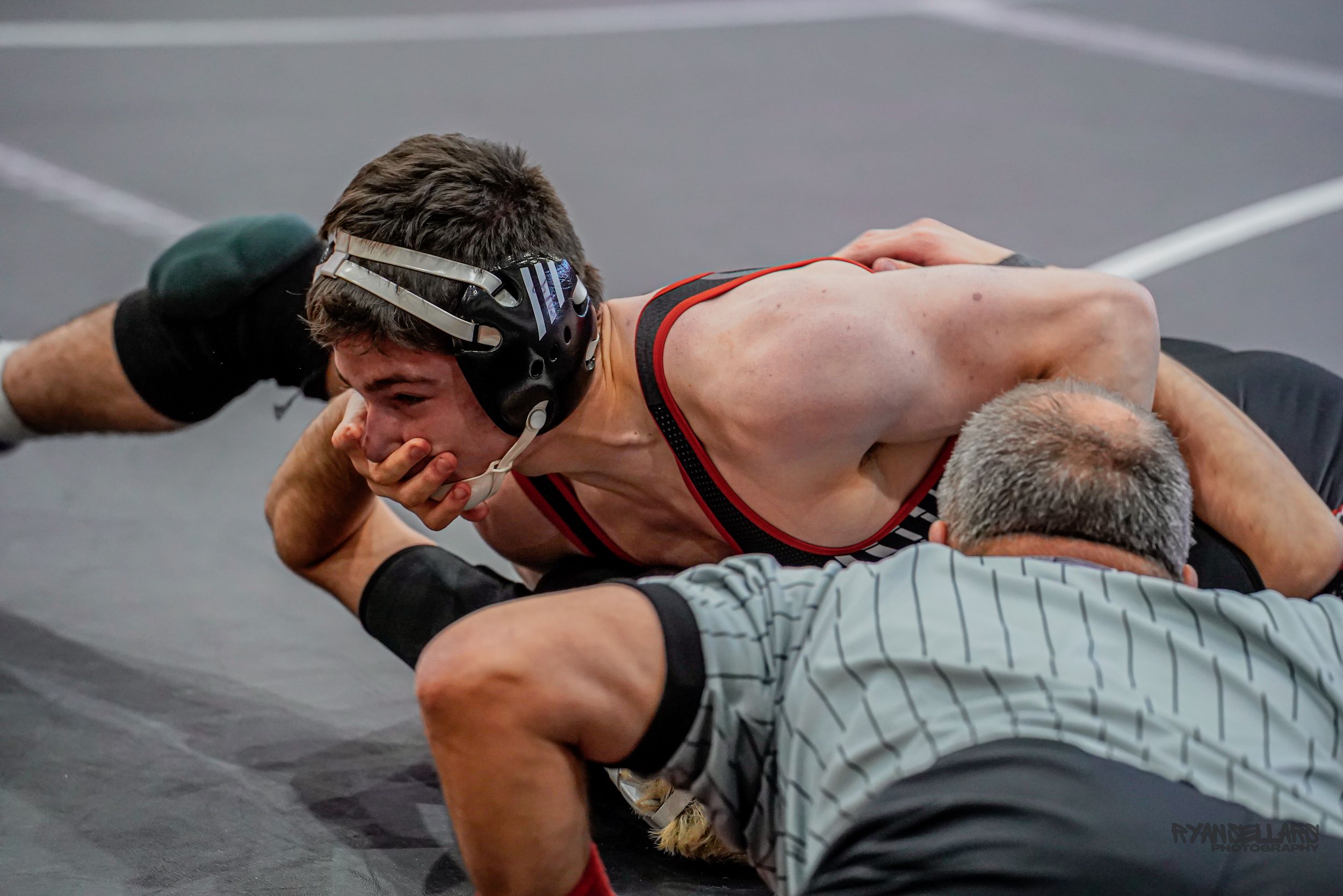 High school wrestlers compete in an intense match on a gray mat as one athlete executes a wrestling hold.