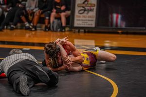 Close-up of wrestling match action on dark mat with competitors engaged in ground techniques.