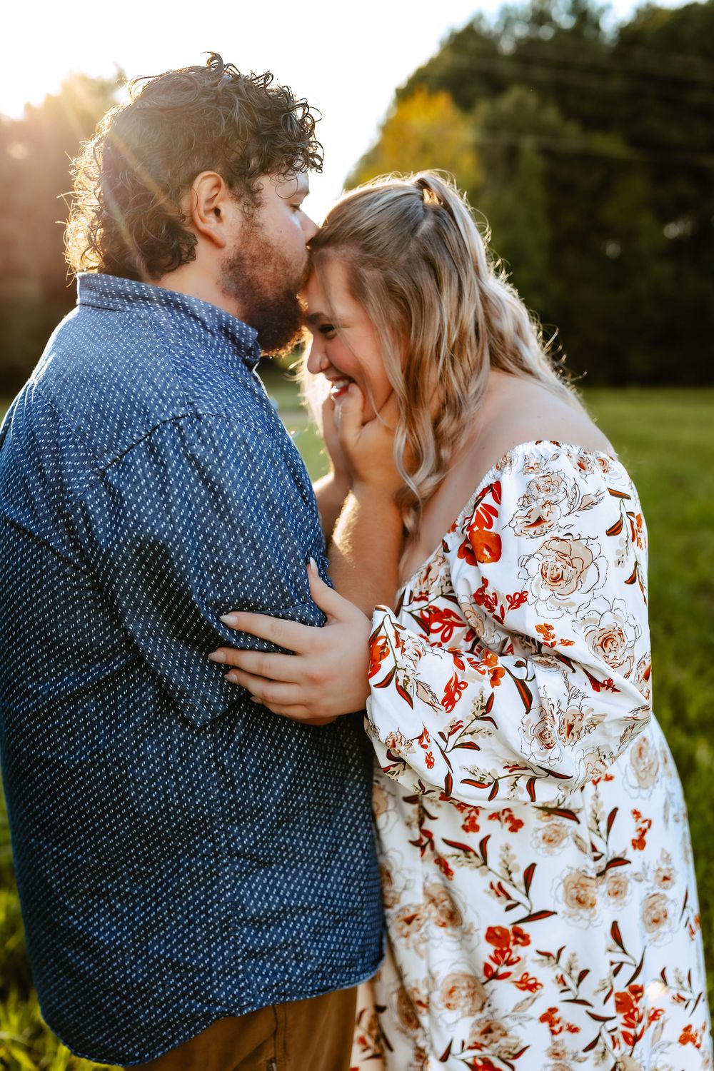 Romantic couple embracing at sunset in a meadow, woman wearing floral dress and man in polka dot shirt.