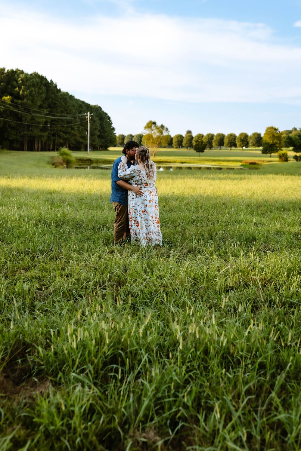 People sharing an intimate moment in a lush green field during golden hour against a bright blue sky.