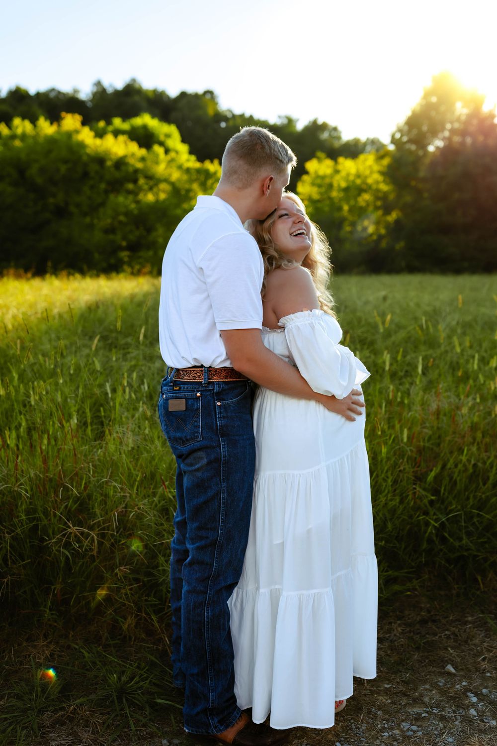 A couple shares an intimate embrace in a golden sunlit meadow during a romantic photoshoot.
