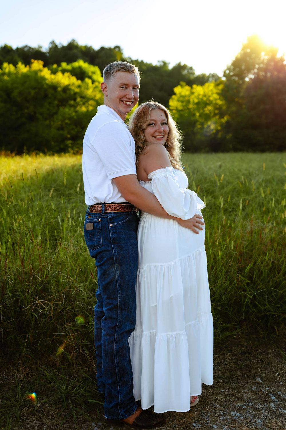 A couple laughing and hugging in a sunlit field during a romantic evening photoshoot.