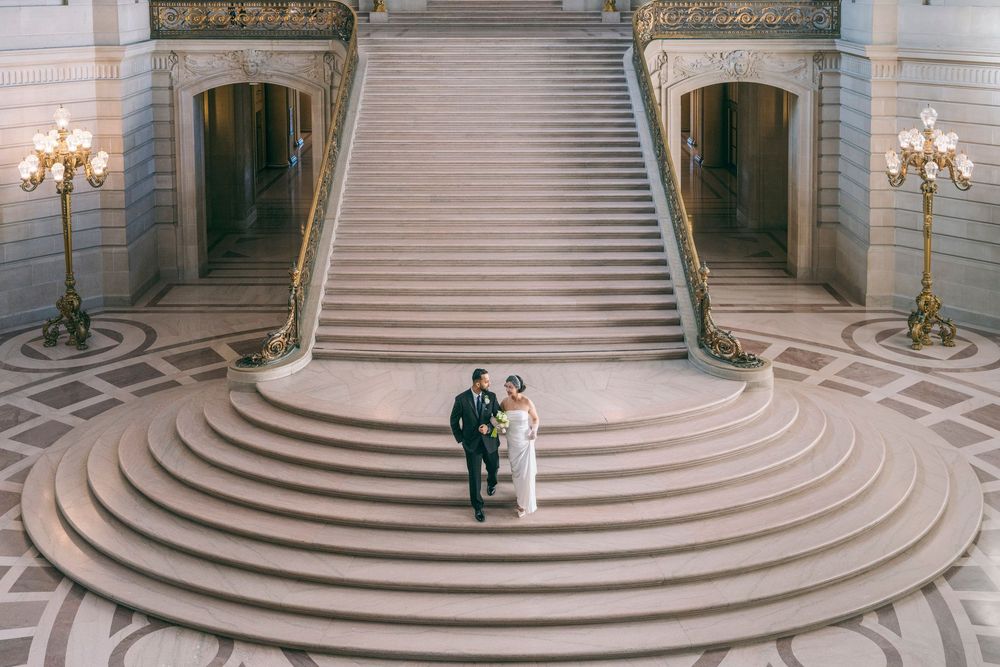 Aerial view of a bride and groom walking down the grand staircase of San Francisco City Hall.