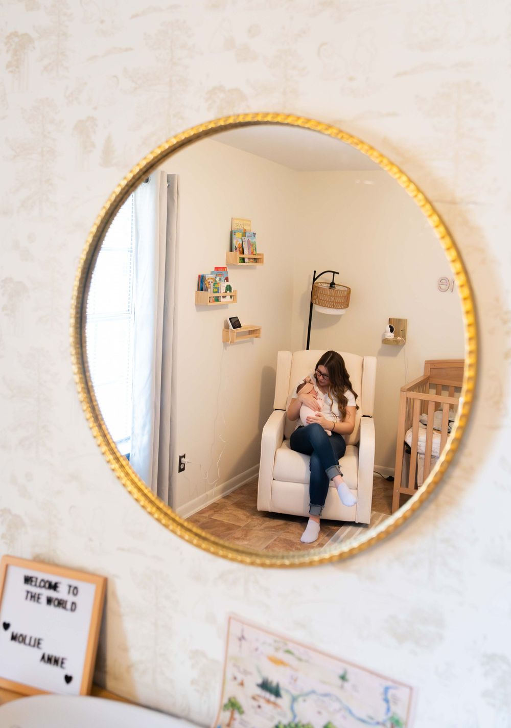 Mirror reflection showing a nursery room with round gold frame and decorative wall art.