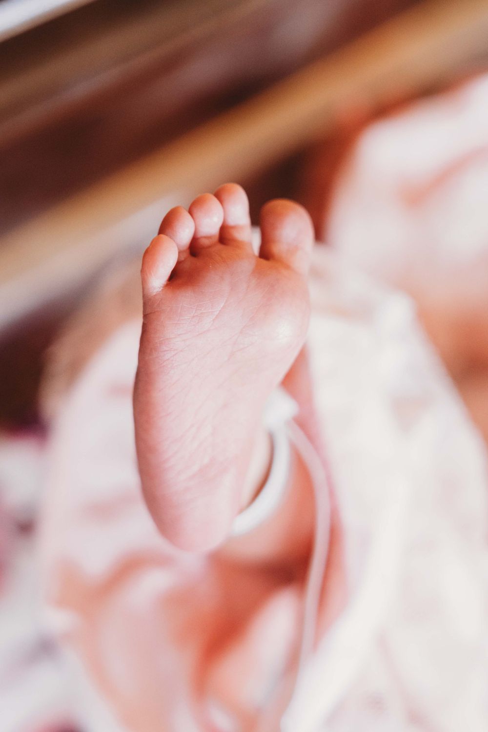 Close-up view of a tiny baby foot against a soft blurred background in warm tones.