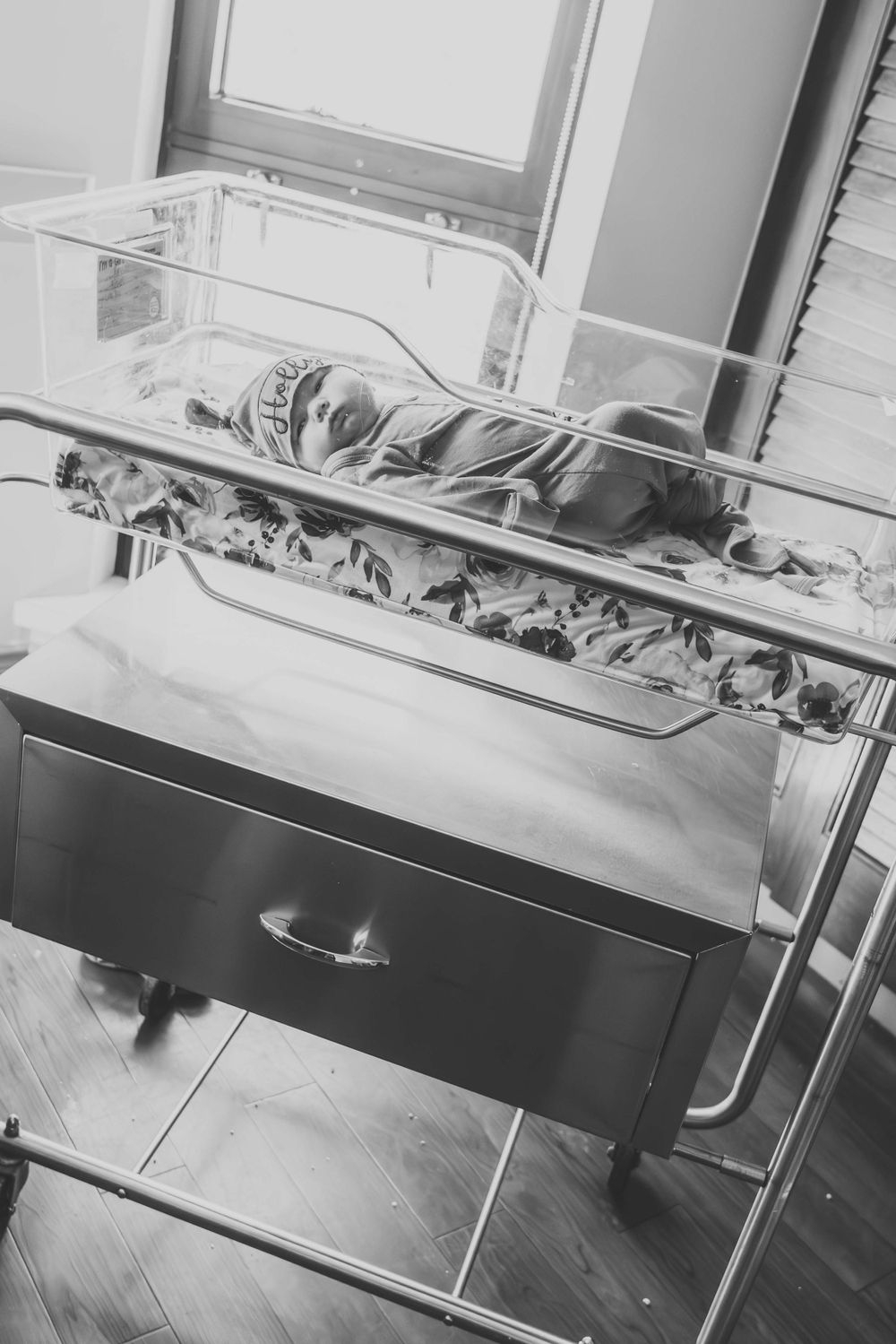 Black and white image of newborn sleeping peacefully in hospital bassinet.
