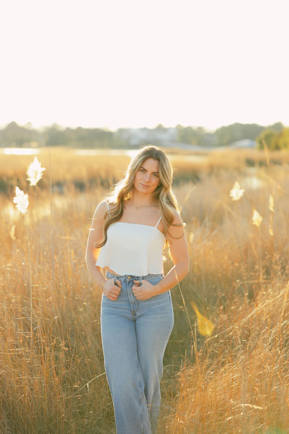 Woman posing in white top and jeans in golden field at sunset.