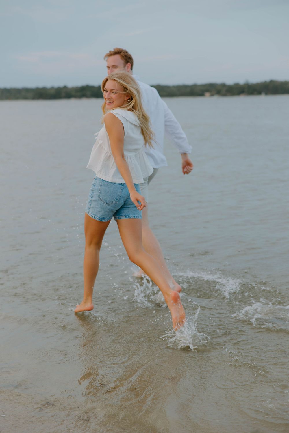 Two people playing and splashing in shallow water at the beach during sunset.