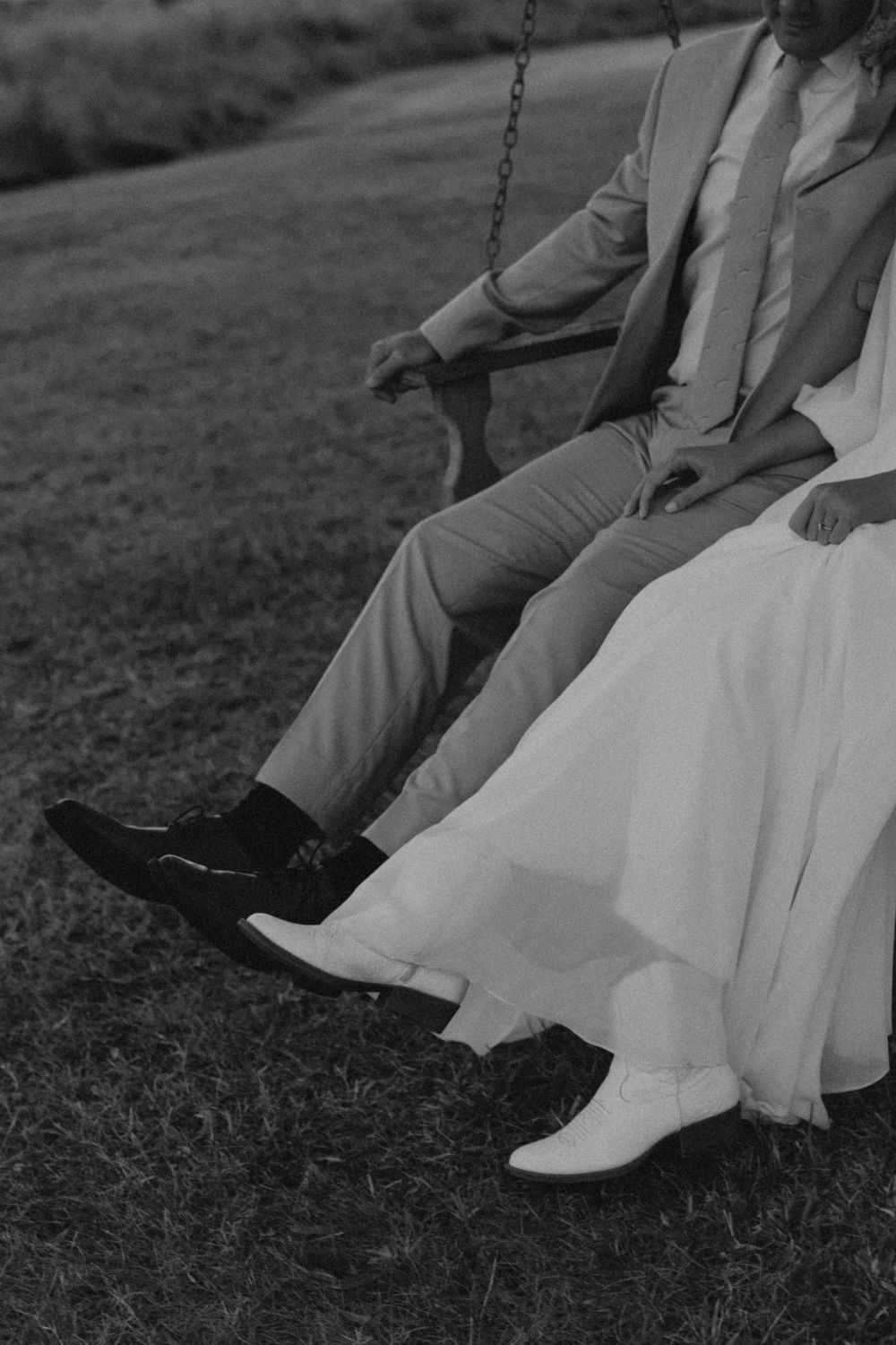 Close-up of bride and groom's feet sitting together on a swing in black and white.