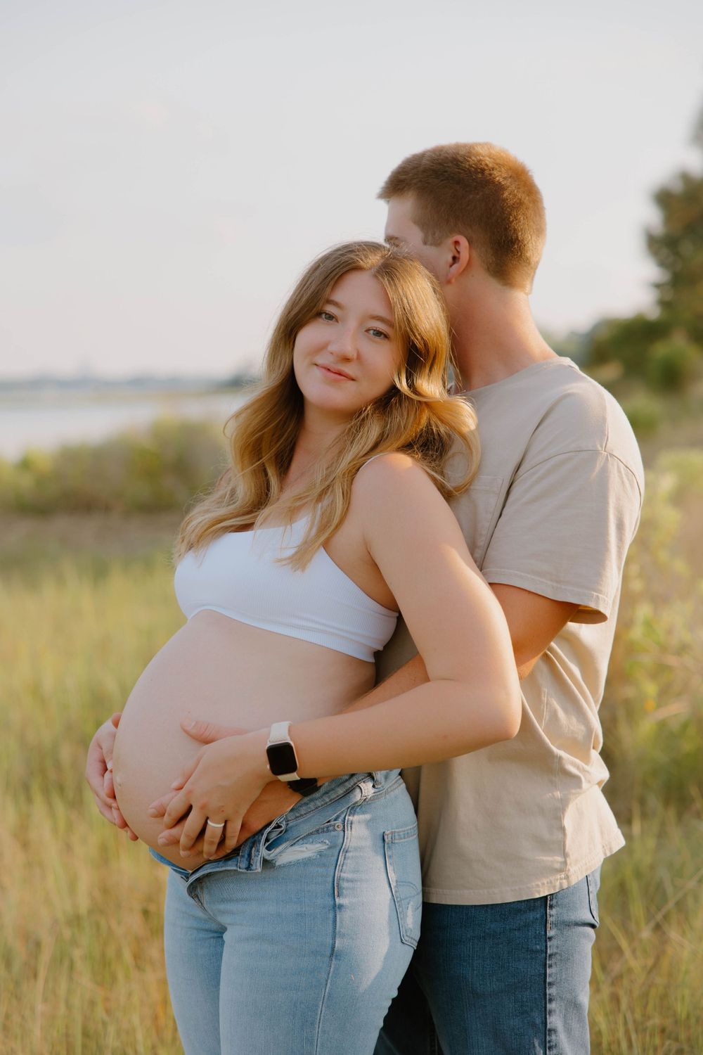 Maternity photo of an expectant couple embracing in a golden field at sunset.