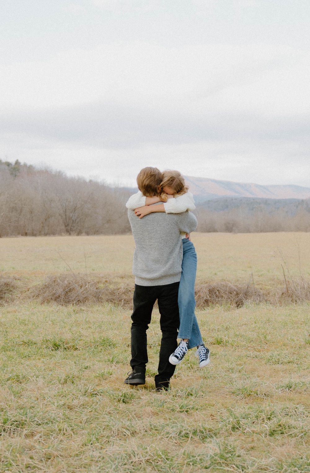 Couple embracing in an open field with mountains in the background.