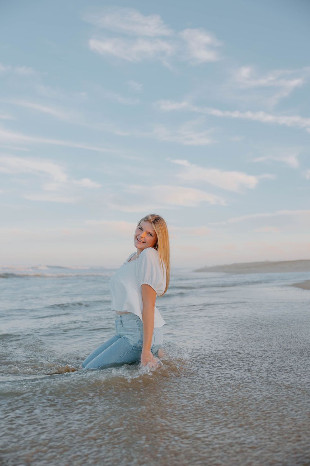 Serene beach photoshoot at sunset with waves lapping at blue jeans.