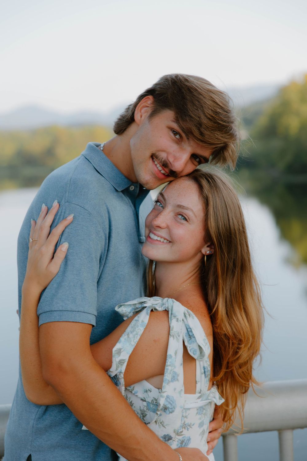 A romantic couple embraces by a lake during sunset.