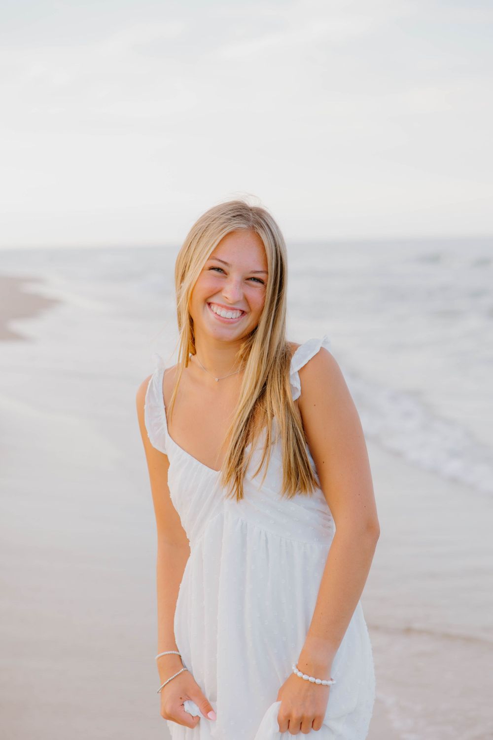 A beach portrait at sunset showing a bright expression and white summer dress.