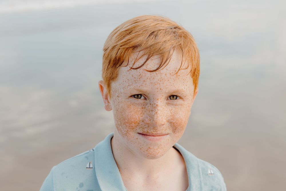 Close-up portrait of a young person wearing a light blue shirt against a soft blurred background.