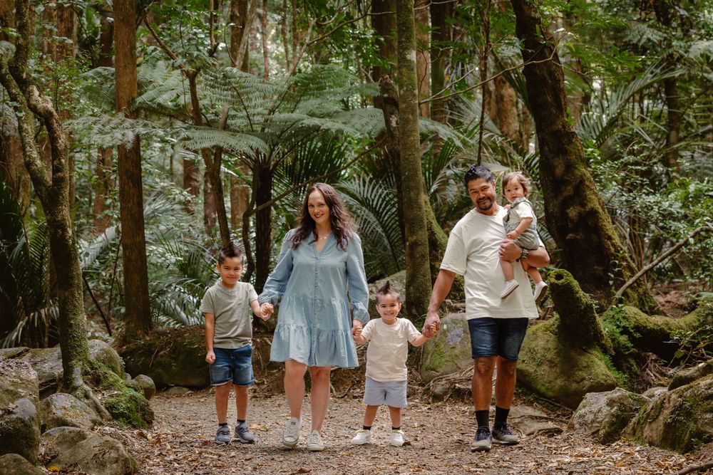 Family walking together on a forest trail surrounded by tall trees and moss-covered rocks.