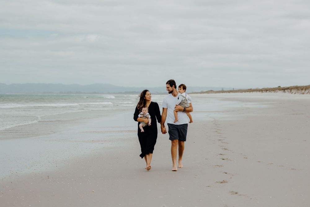 Couple walking along a serene beach shoreline under cloudy skies.