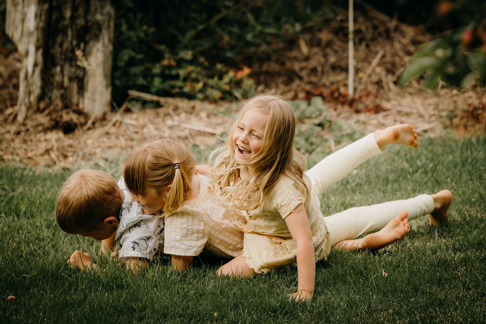 Children playing and laughing together while lying on green grass in a backyard setting.