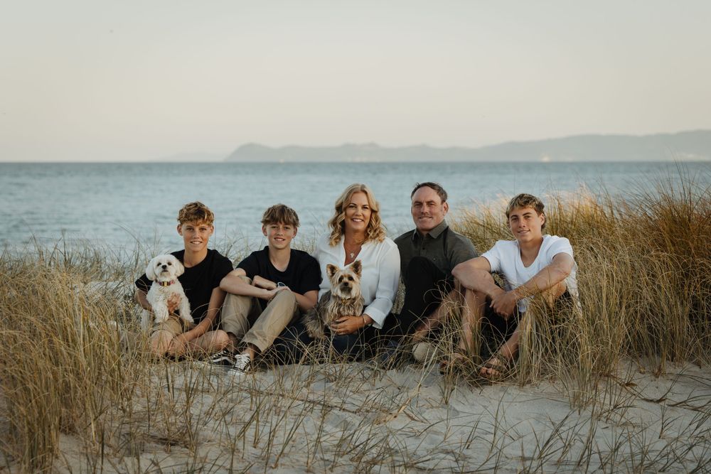 Family and their dogs sitting together on a coastal sand dune at sunset.
