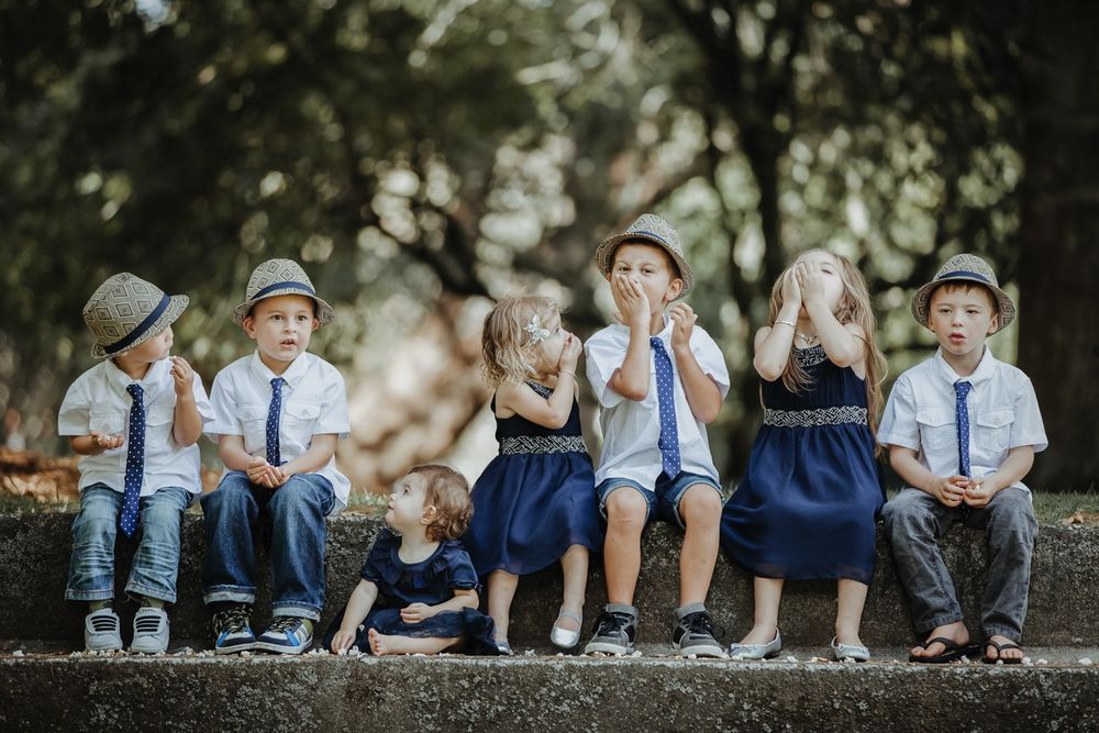 Children in coordinated blue and white outfits sitting on log making silly faces.