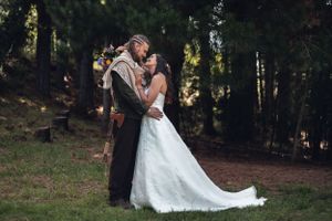 A couple in wedding attire share an intimate moment in a sunlit forest setting during their outdoor ceremony.