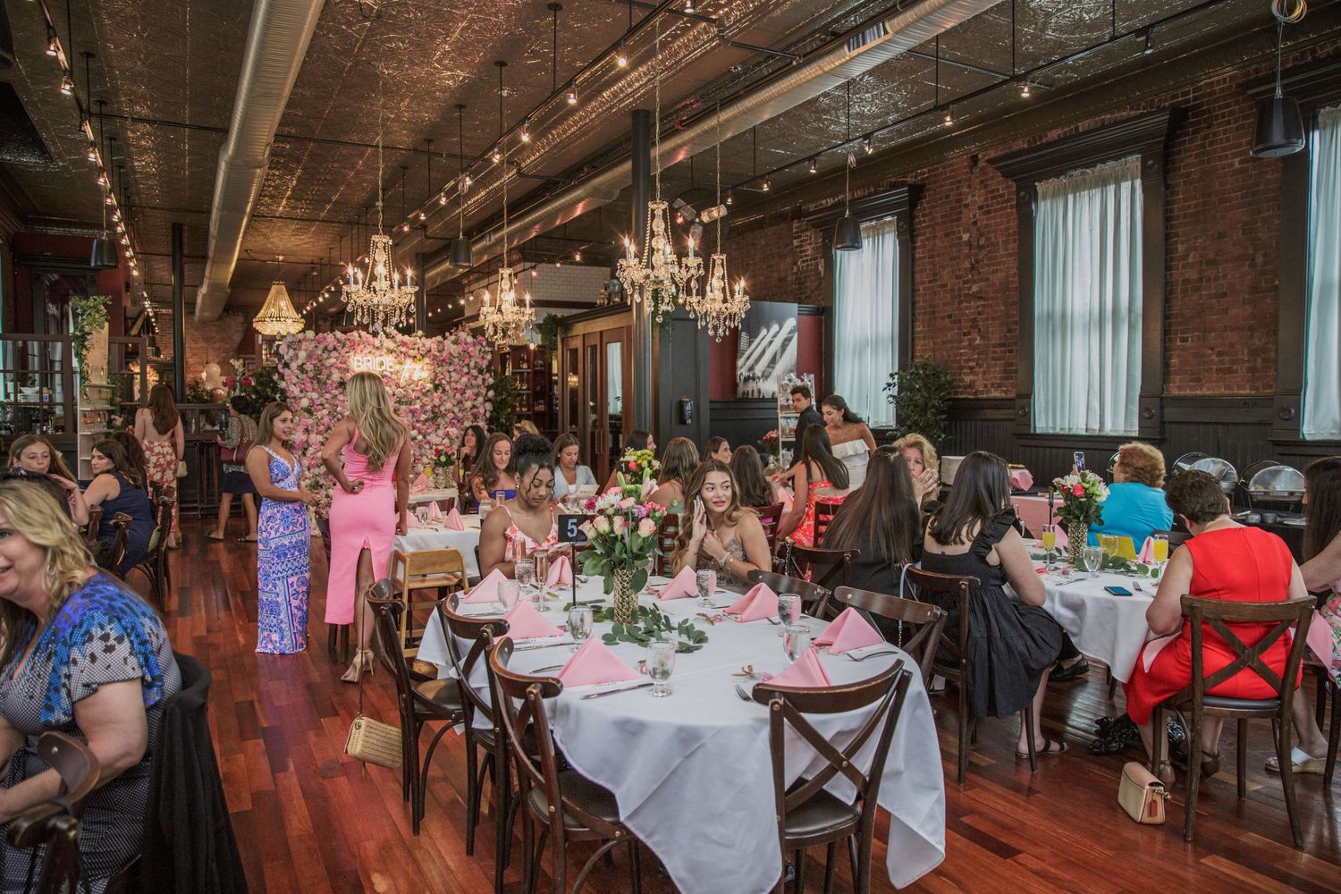 Elegant dining room with exposed brick walls, ornate chandeliers, and tables set for a special event reception.