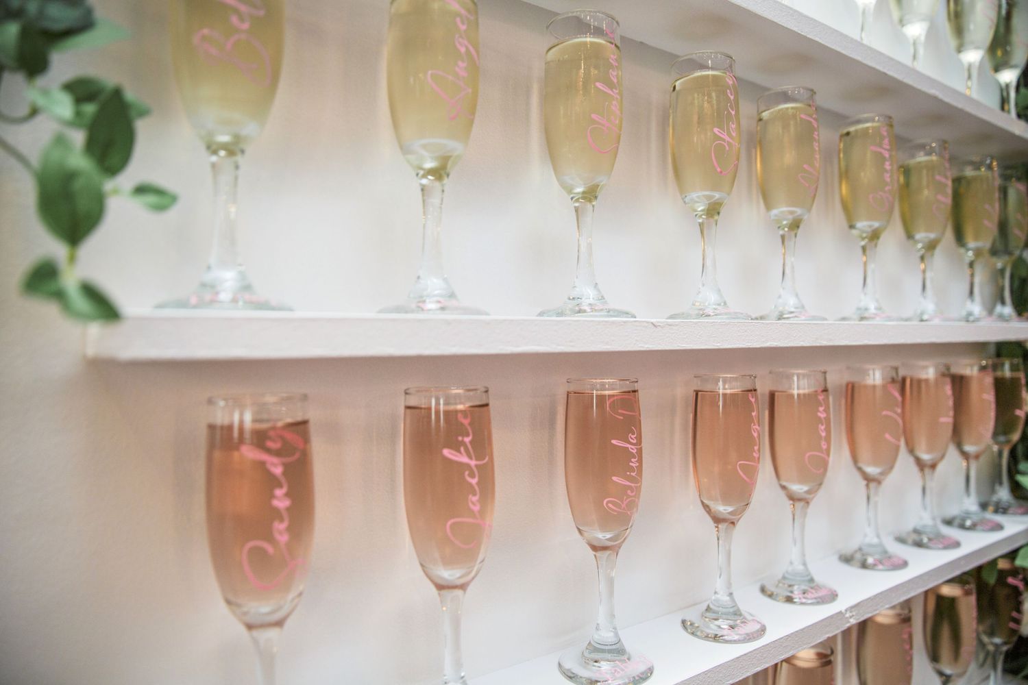 Rows of champagne flutes filled with golden and rose-colored bubbly beverages arranged on white shelves.