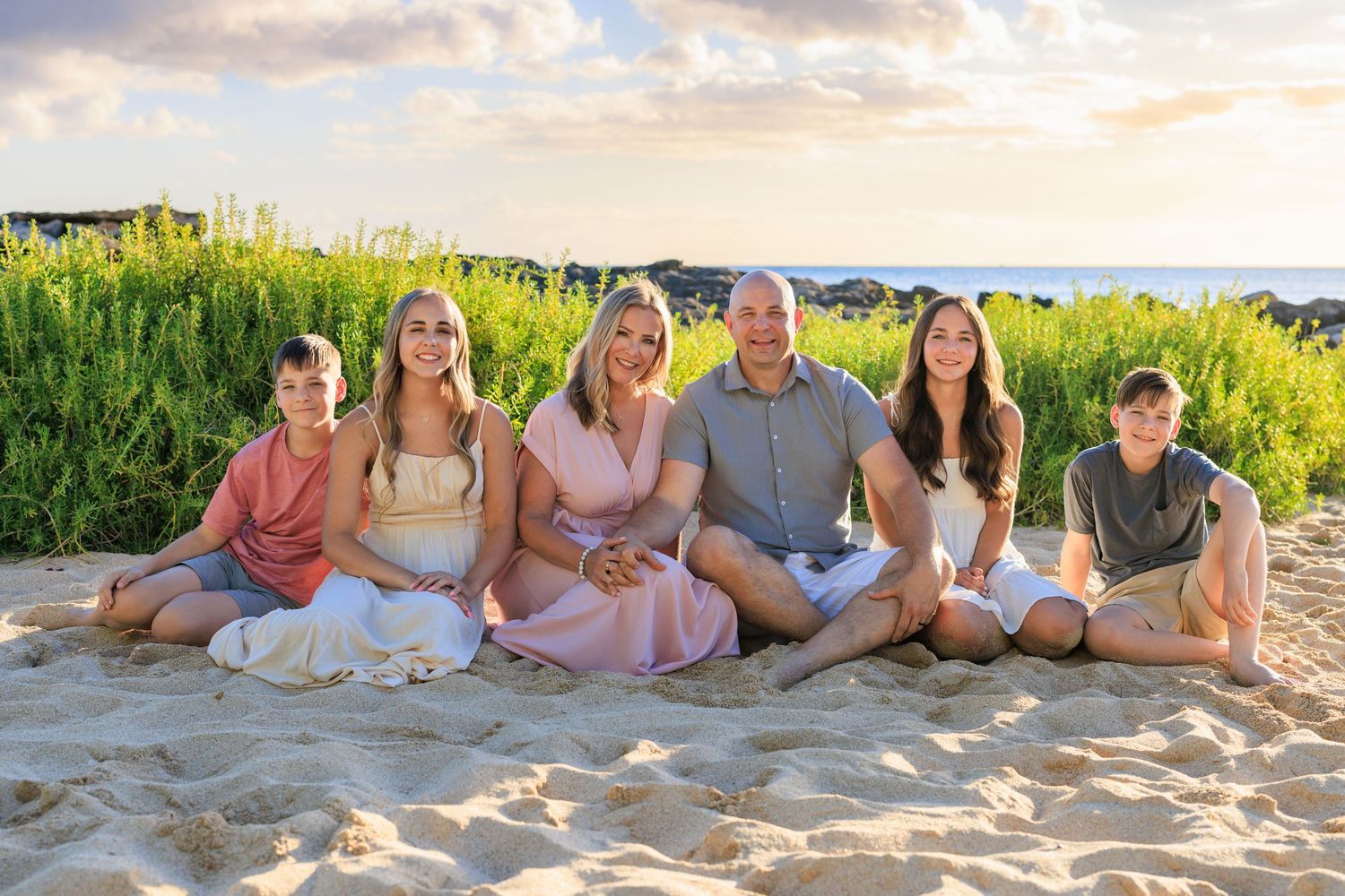 Family of four posing in lush green meadow with dramatic mountain backdrop at sunset in Hawaii.