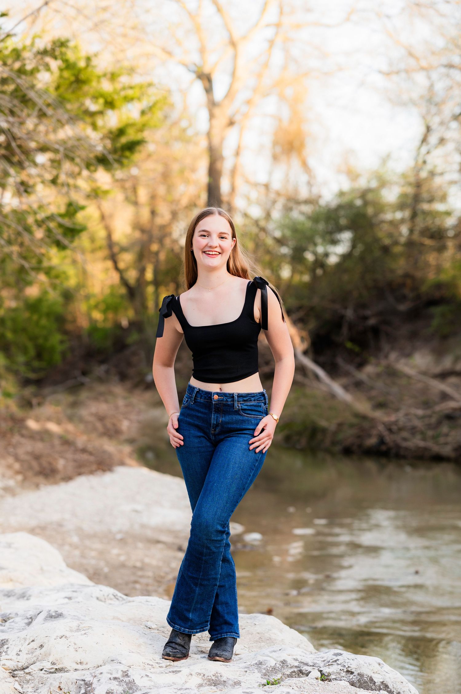 Senior poses on the bank of a creek during senior photo session by mesquite, tx family photographer