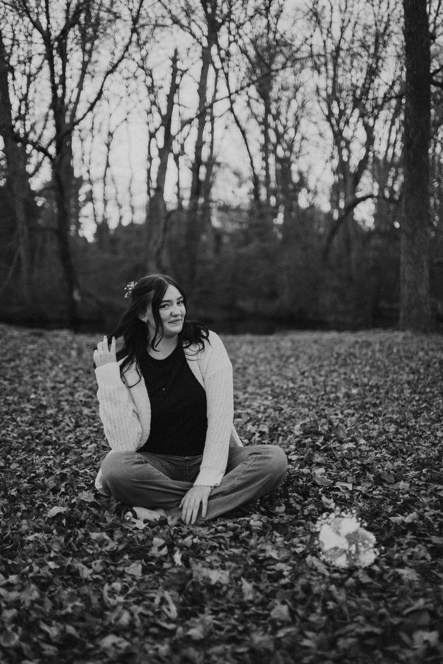 A black and white portrait session in a leaf-covered forest setting.