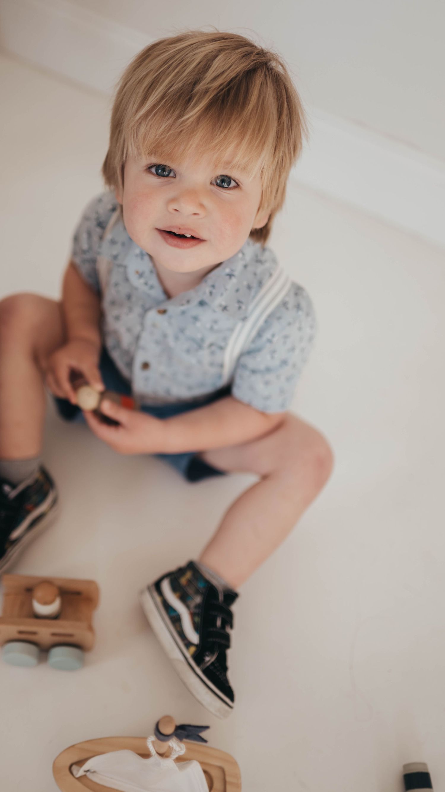 Baby in a floral outfit crawls on white surface next to shoes.