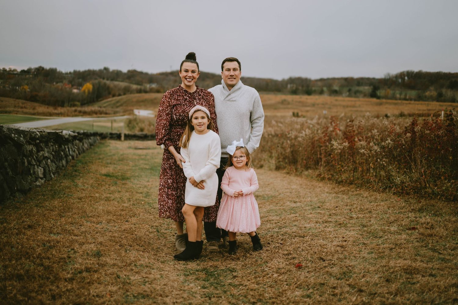 A group of people walk together through a golden autumn field during a photo session at sunset.