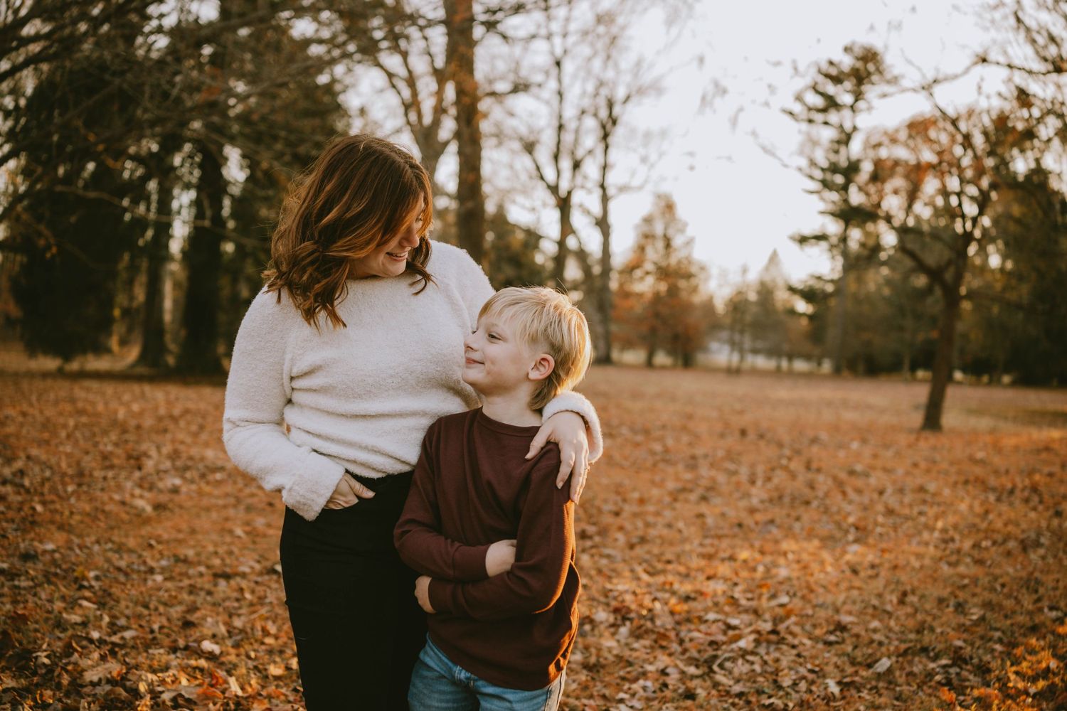 A mother and young child share a tender moment in an autumn park surrounded by fallen leaves.
