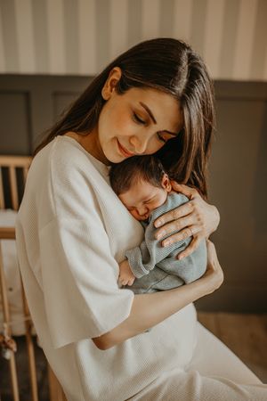A tender moment captured in warm light as parent cradles sleeping newborn baby while wearing cream colored sweater.
