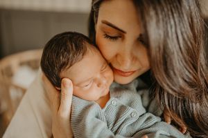 Tender moment between mother and sleeping newborn baby in soft sweater captured in warm lighting.