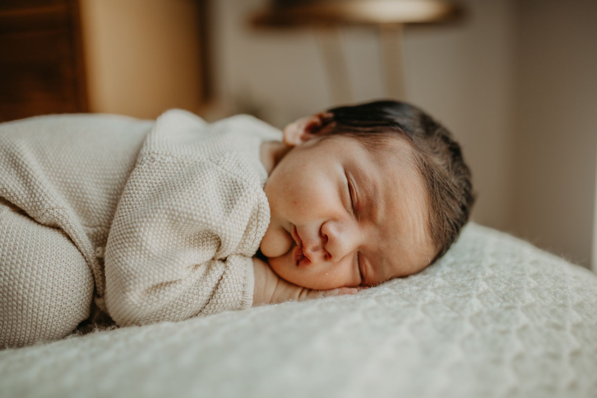 A sleeping newborn wrapped in a cream-colored knit blanket rests peacefully on textured bedding.