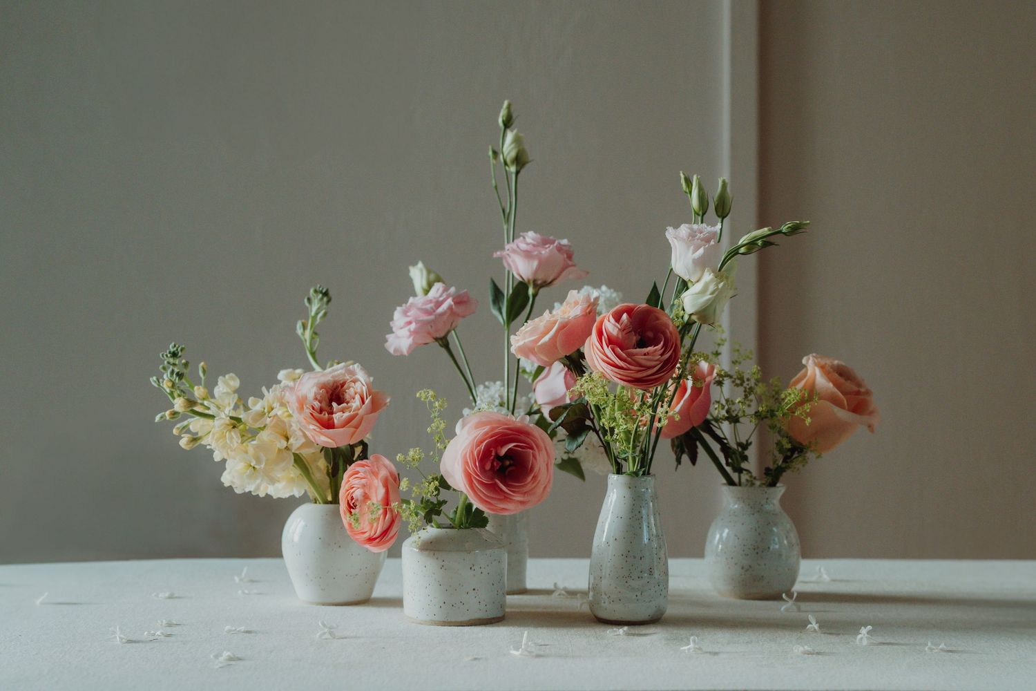 Elegant wedding table centerpiece featuring pink ranunculus and roses arranged in small white ceramic vases. Victoria, BC, Vancouver Island.