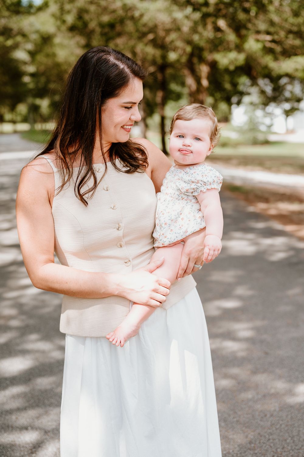 Mother and baby in matching white outfits share a tender moment outdoors on a sunny day.