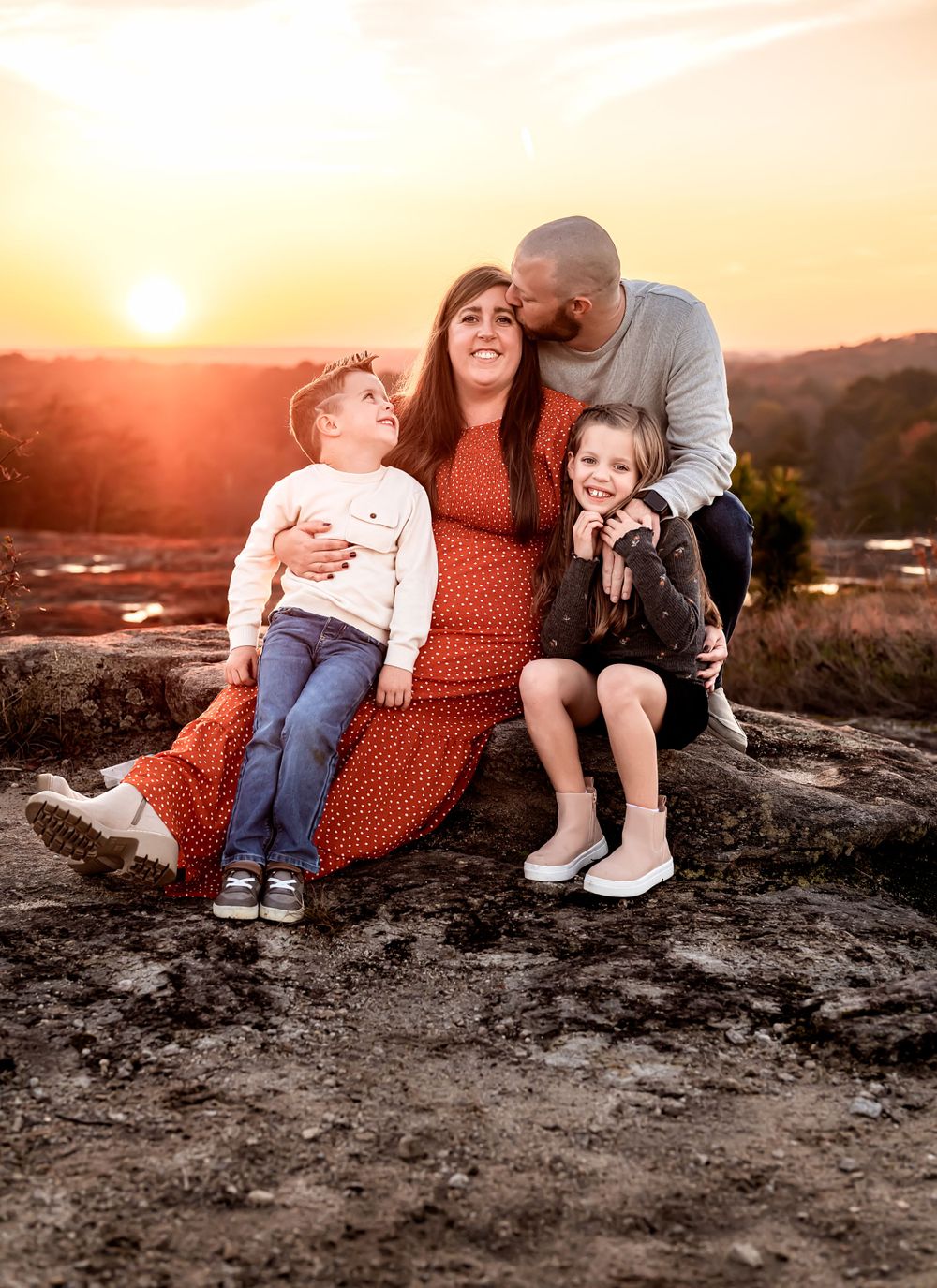 Family sitting together on rocky outcrop during golden sunset.