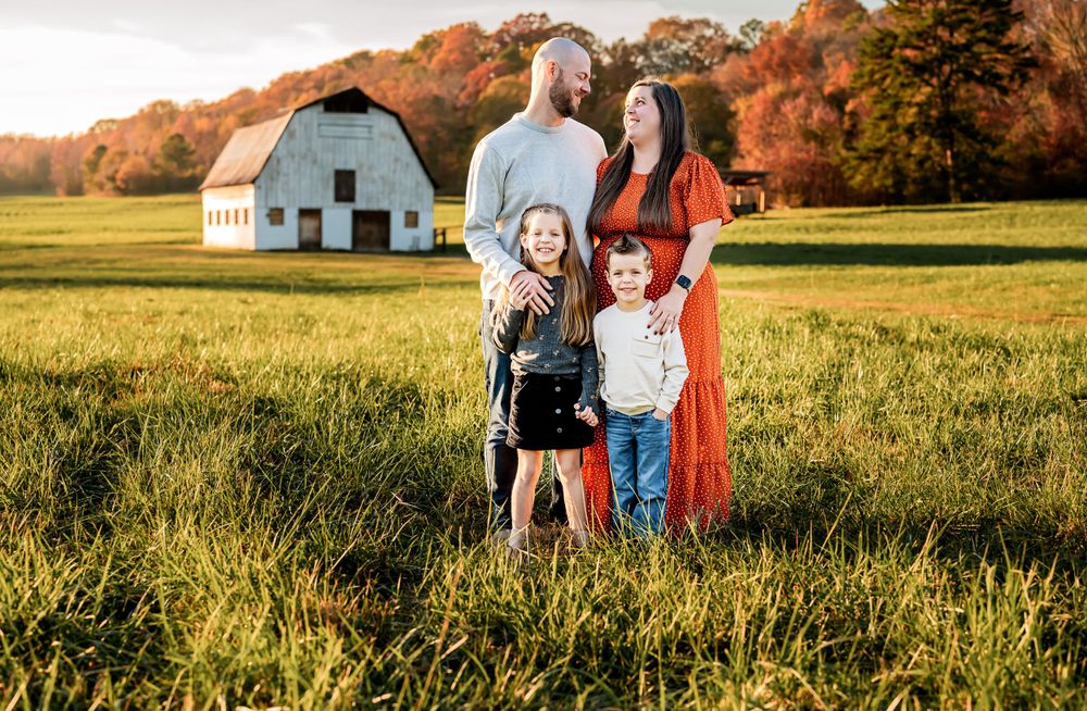 Family portrait in front of rustic barn during autumn golden hour.