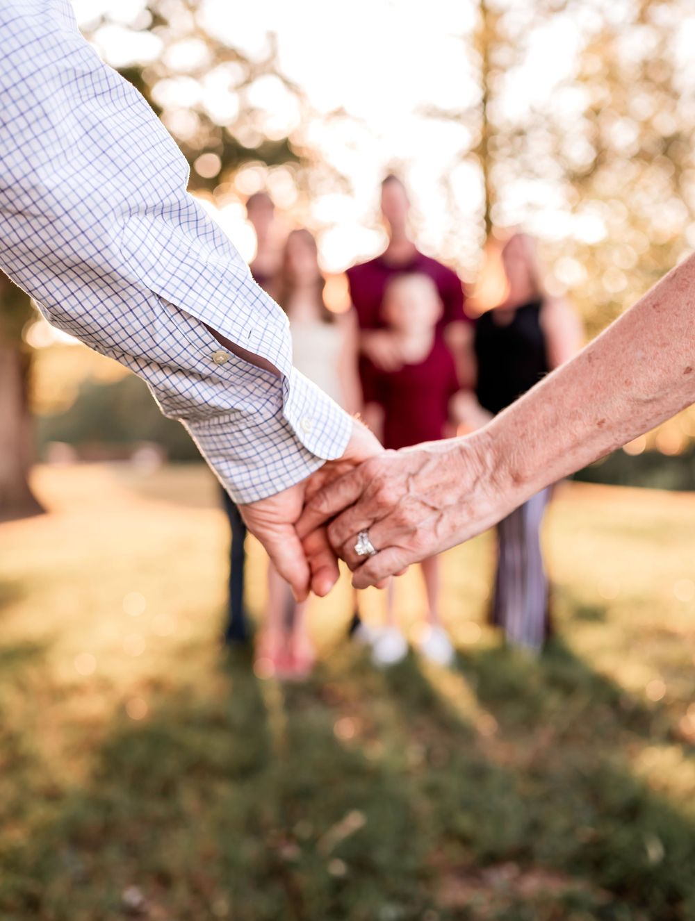 Close-up of two hands holding each other with wedding rings in golden sunset light.