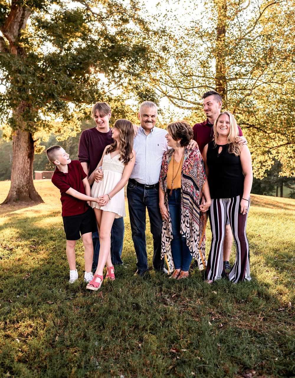 Family portrait session on grassy hill with trees in background during sunset.