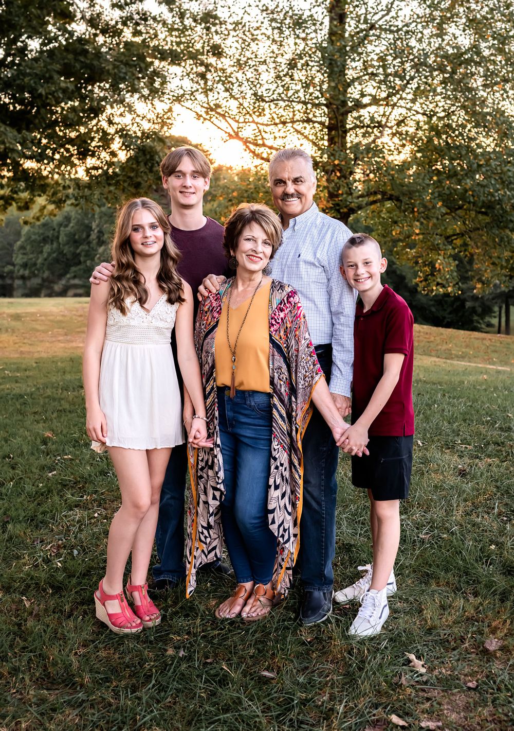 Family group portrait with sunset light filtering through trees in background.