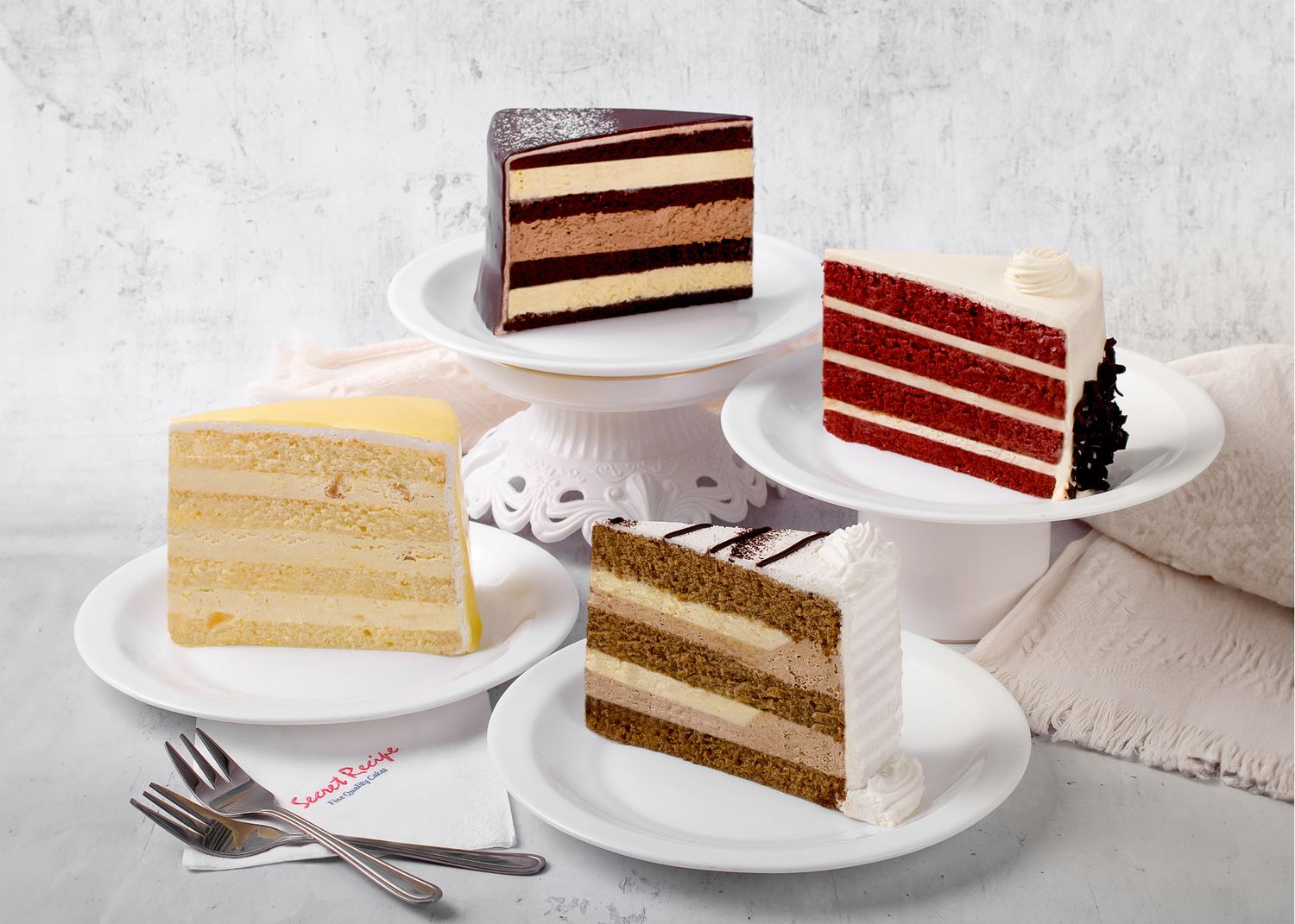 Assorted layered cake slices on white plates including chocolate and vanilla varieties.