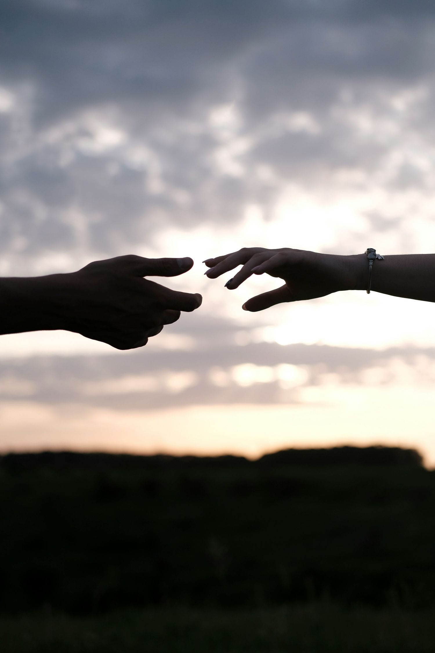 Silhouetted hands reaching toward each other against a dramatic sunset sky.