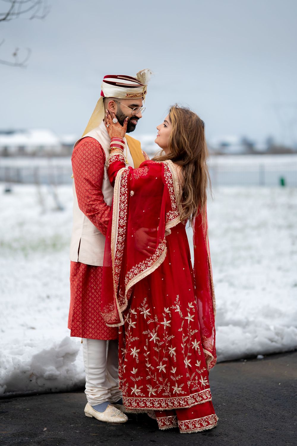 A couple in traditional Indian wedding attire poses against a snowy winter backdrop.
