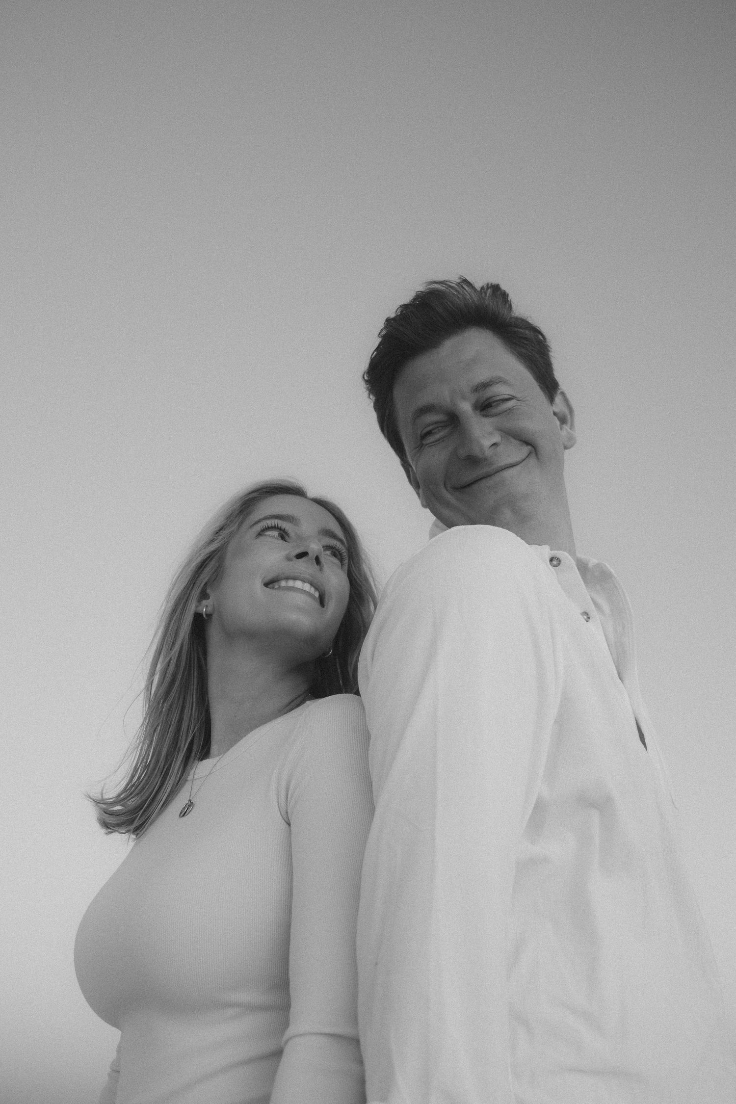 Couple smiling while posing back to back in black and white portrait.